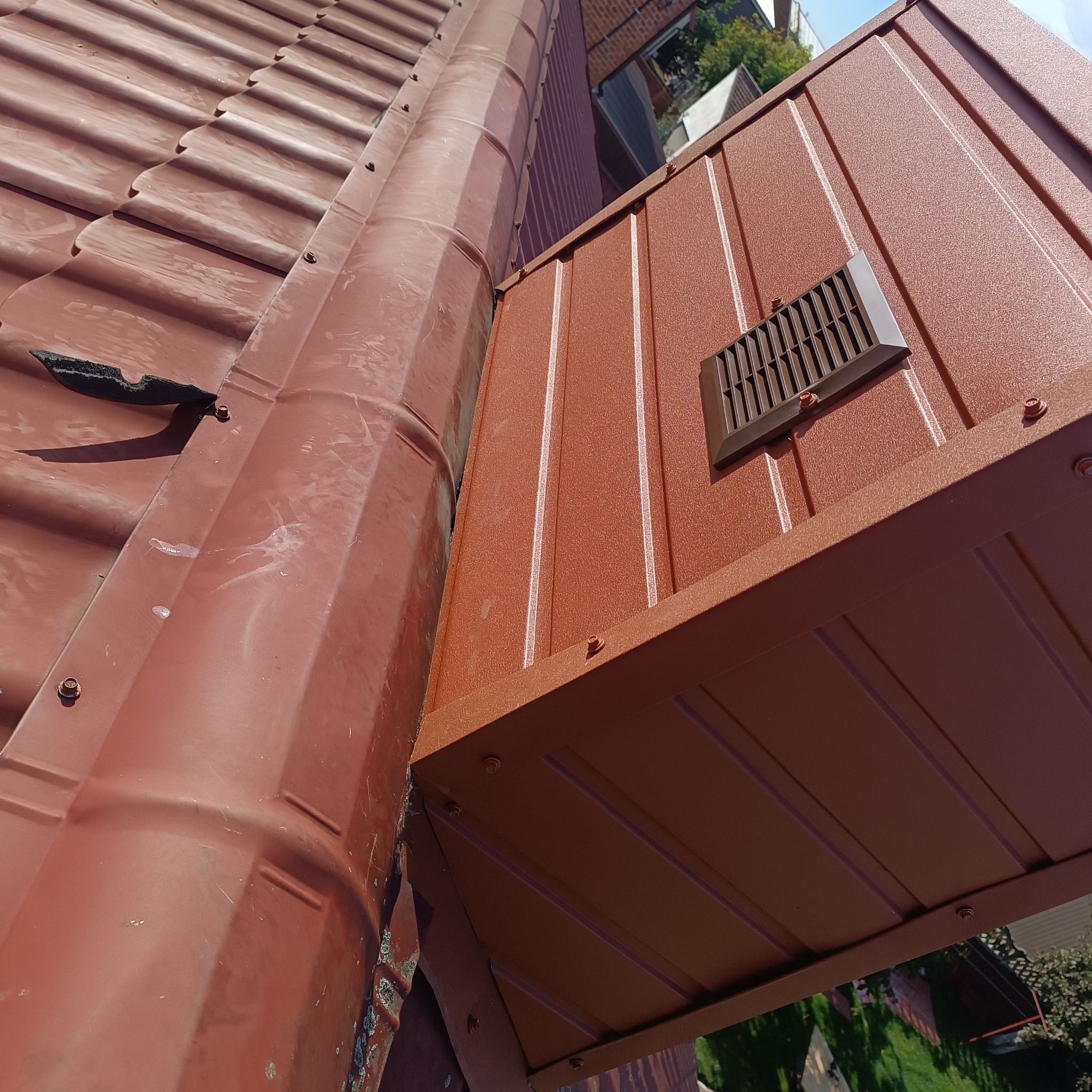 Brązowy dach z blachy trapezowej z zamontowanym wywietrznikiem dachowym. Widoczne mocowania i uszczelki. Ujęcie z dołu.
