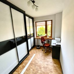 DOMIBUD Usługi Remontowo - Budowlane Robert Brzykcy - Pokój z dużym przesuwnym szafą z czarno-białymi frontami, biurkiem przy oknie, krzesłem biurowym i parkietem w jodełkę; widoczna listwa przypodłogowa przed szafą.
