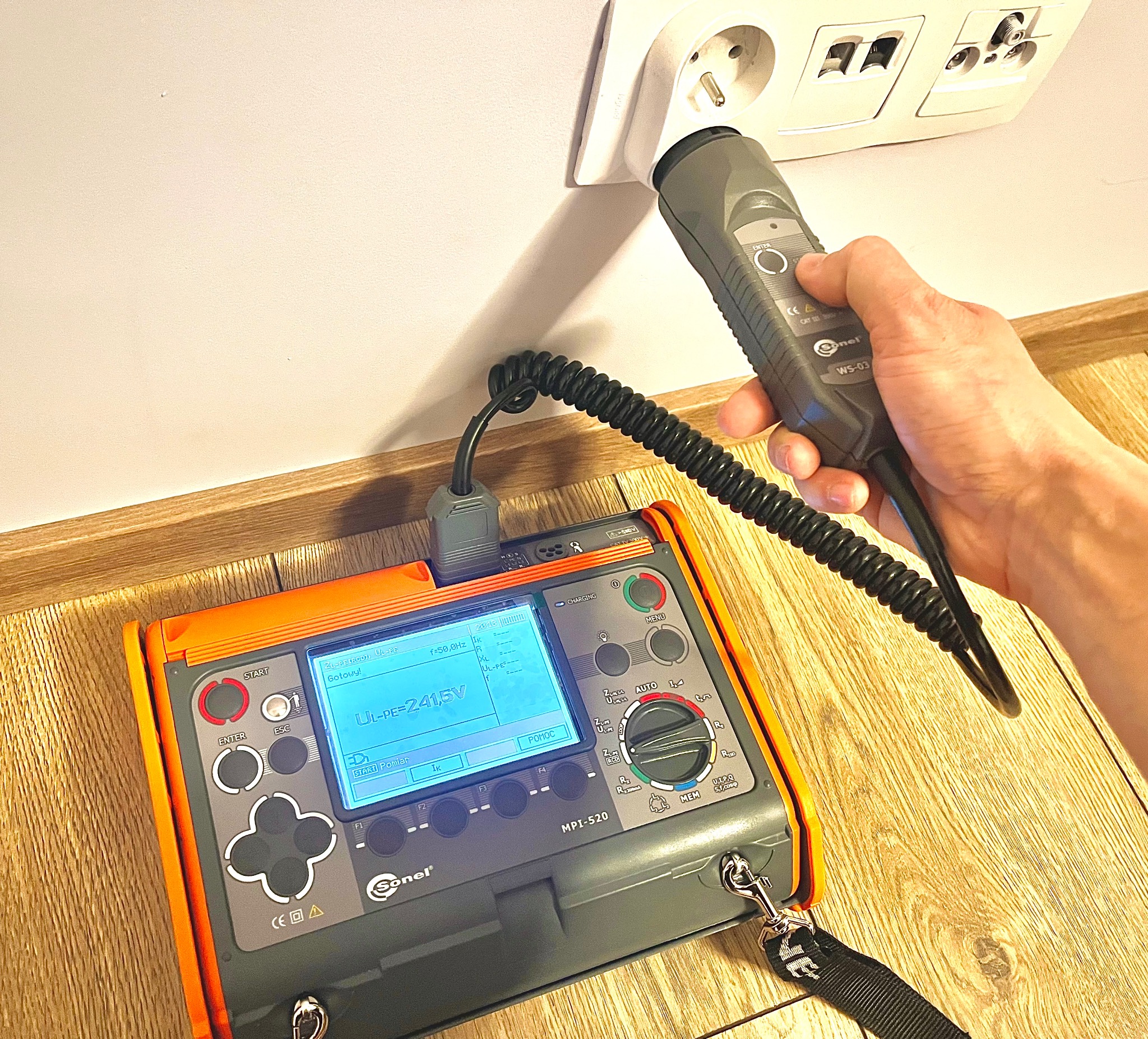 Pomiar napięcia w gniazdku elektrycznym za pomocą miernika Sonel MPI-520 i wskaźnika WS-03, widoczny wyświetlacz urządzenia z wartością napięcia UL-PE=241,5V.