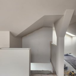 Piotr Turkiewicz - Wnętrze poddasza w trakcie prac wykończeniowych, widoczne świeżo pomalowane ściany i sufit, zabezpieczona podłoga, widoczne przewody elektryczne i schody w stanie surowym.