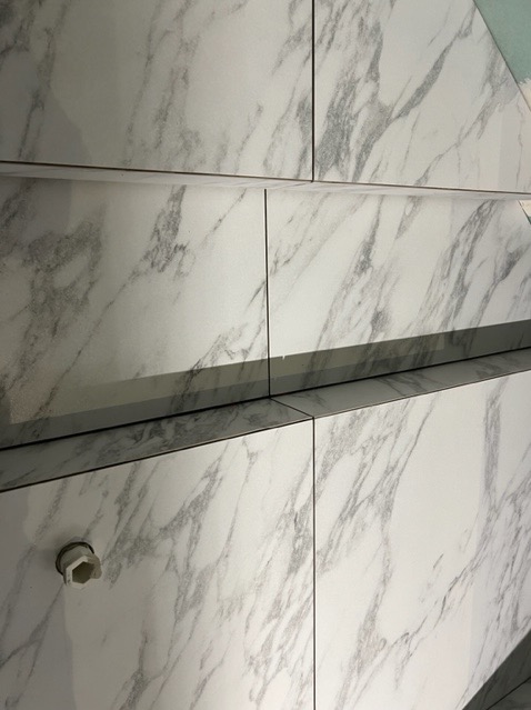 Białe płytki imitujące marmur na ścianie, widoczny fragment instalacji hydraulicznej z plastikową zaślepką