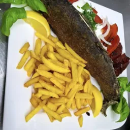 Usmażony pstrąg z frytkami, cytryną i warzywami na białym talerzu. Danie gotowe do spożycia, z bliska, na metalowym blacie.