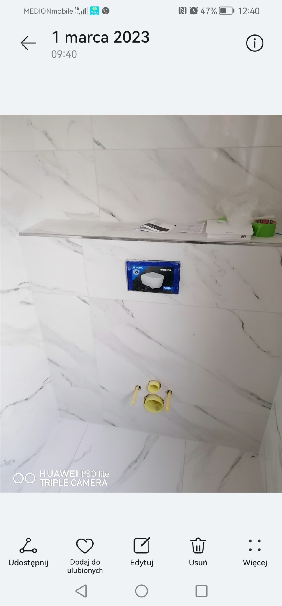 Świeżo wykafelkowana ściana w łazience z marmurowym wzorem, z zamontowaną spłuczką podtynkową Geberit w oryginalnym opakowaniu i przygotowanymi przyłączami kanalizacyjnymi.