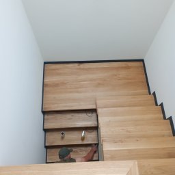 Bartłomiej Godzinski - Montaż drewnianych schodów z czarnymi akcentami; widoczny pracownik w trakcie wykańczania detali.