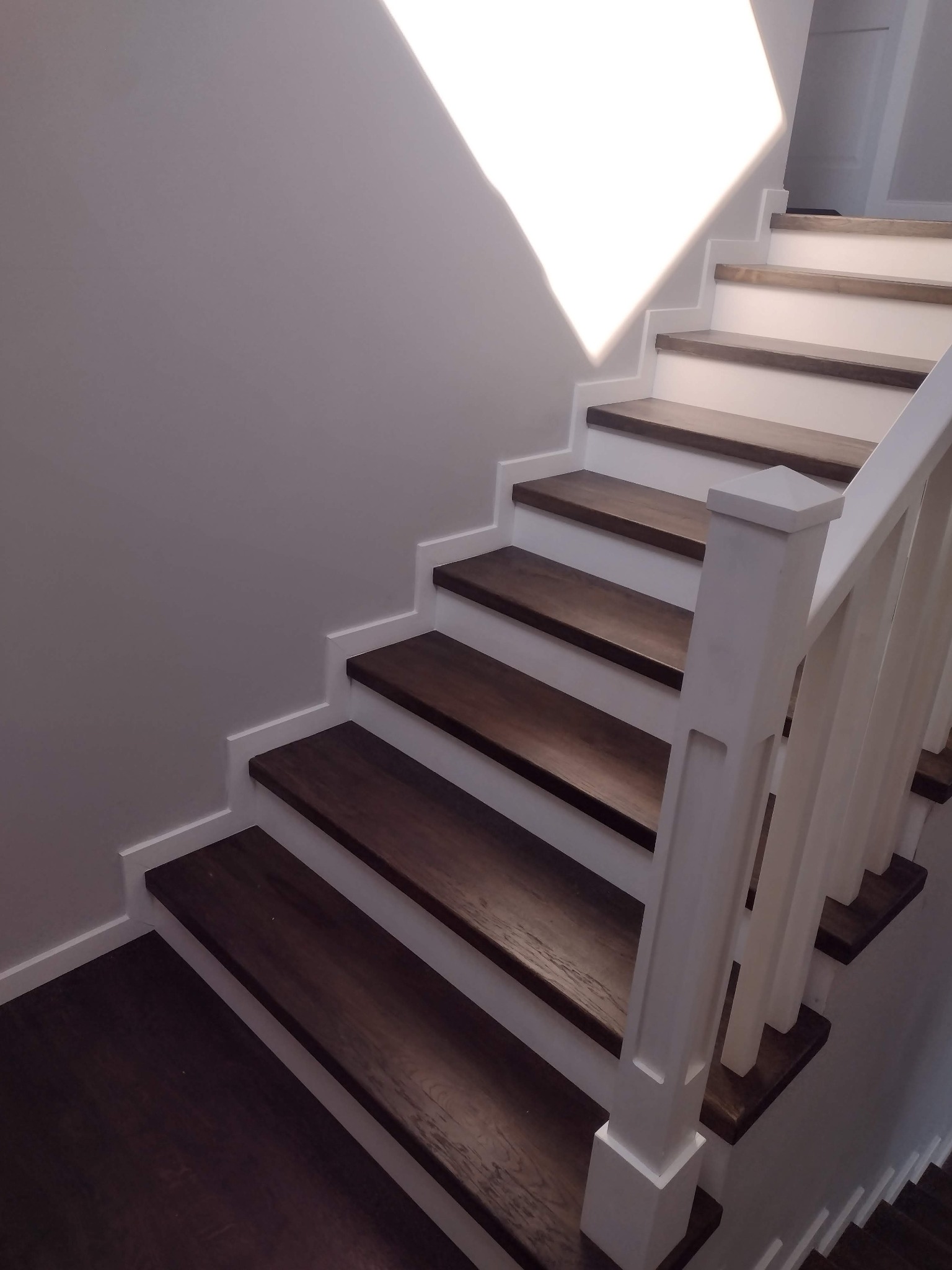 Nowoczesne schody z ciemnego drewna i białymi elementami, oświetlone naturalnym światłem wpadającym z góry.