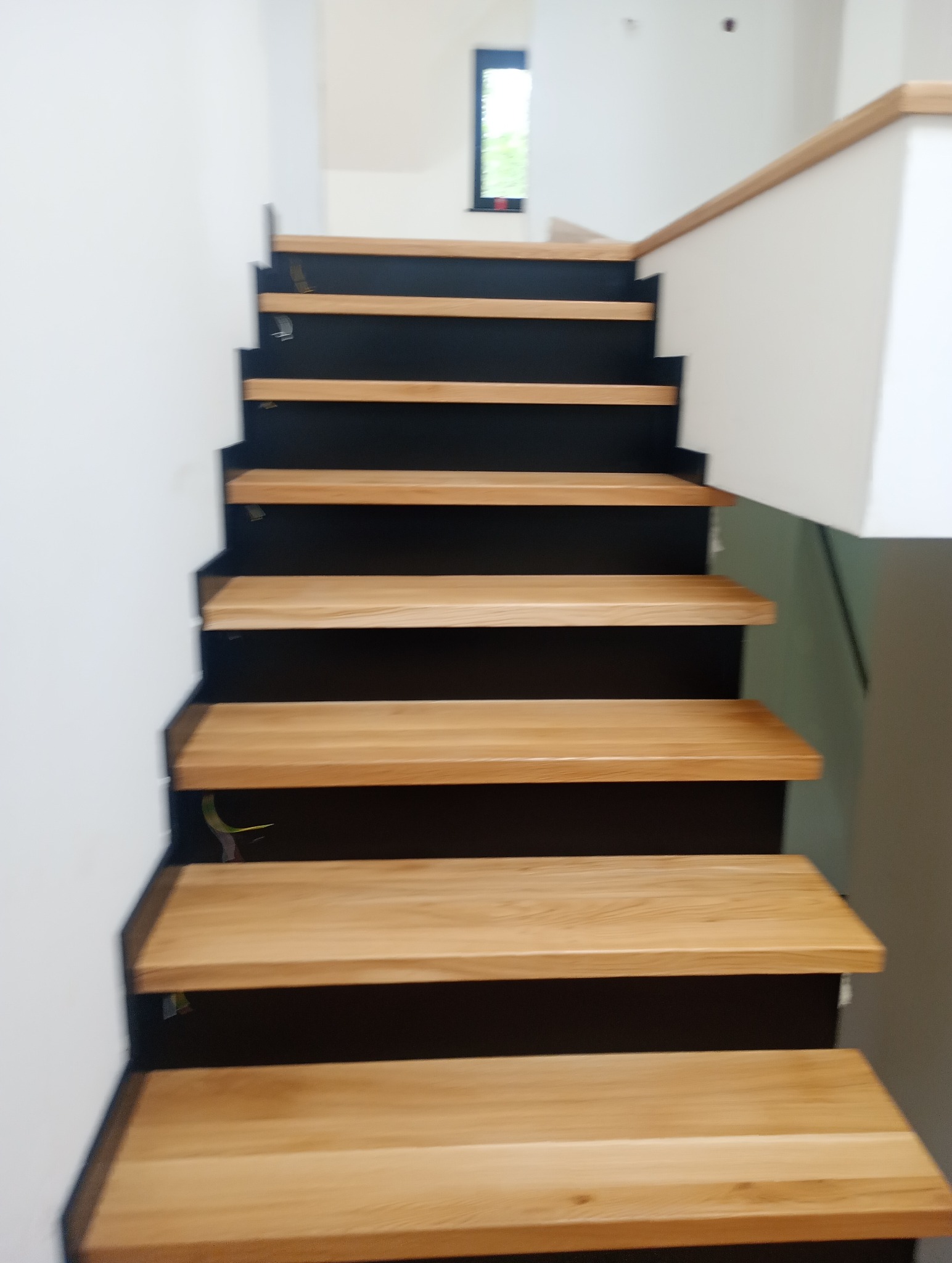 Nowoczesne schody drewniane z czarnymi podstopnicami i jasnym drewnem na stopniach, widok z dołu.