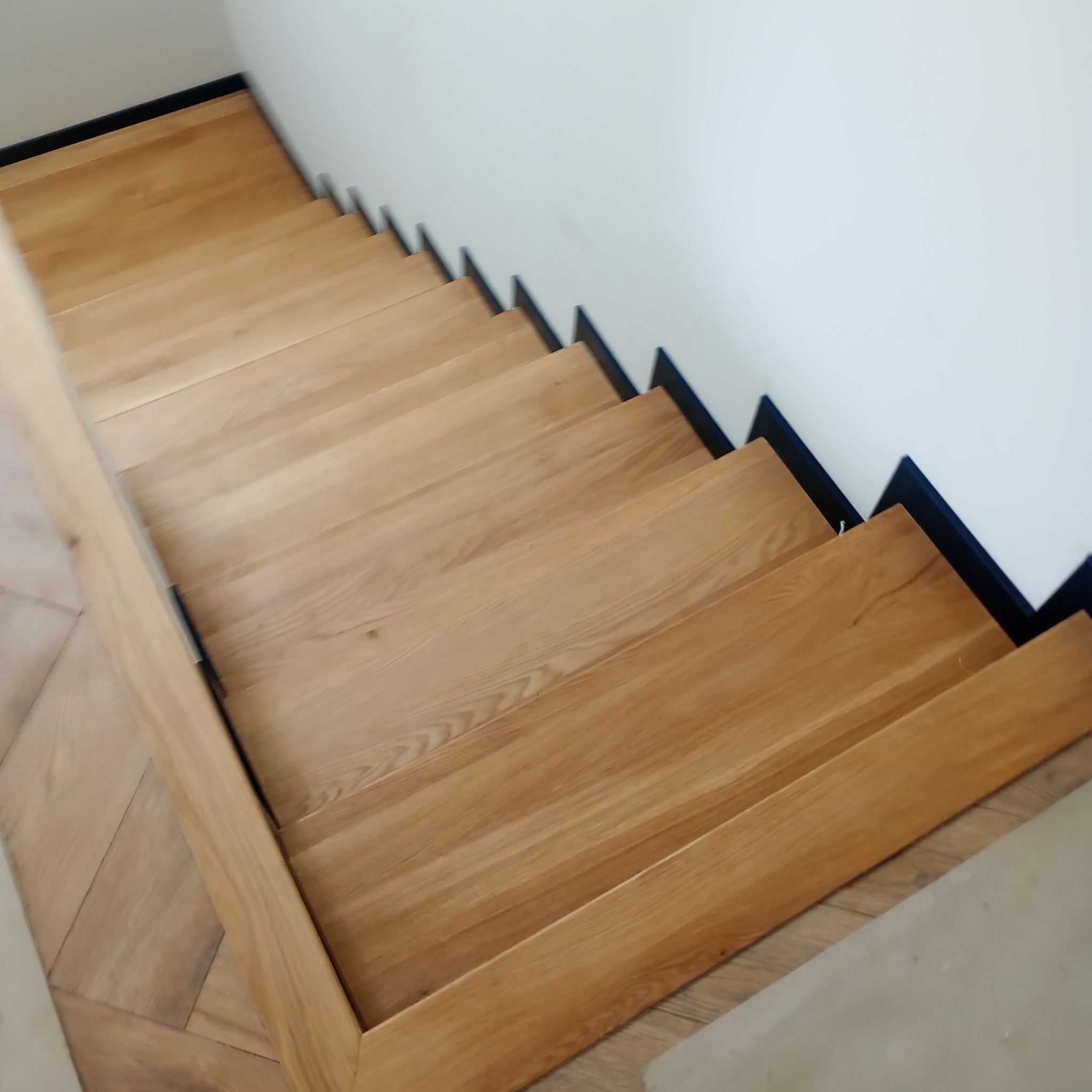 Nowoczesne schody z jasnego drewna z czarnymi podstopnicami, widok z góry, minimalistyczny design.