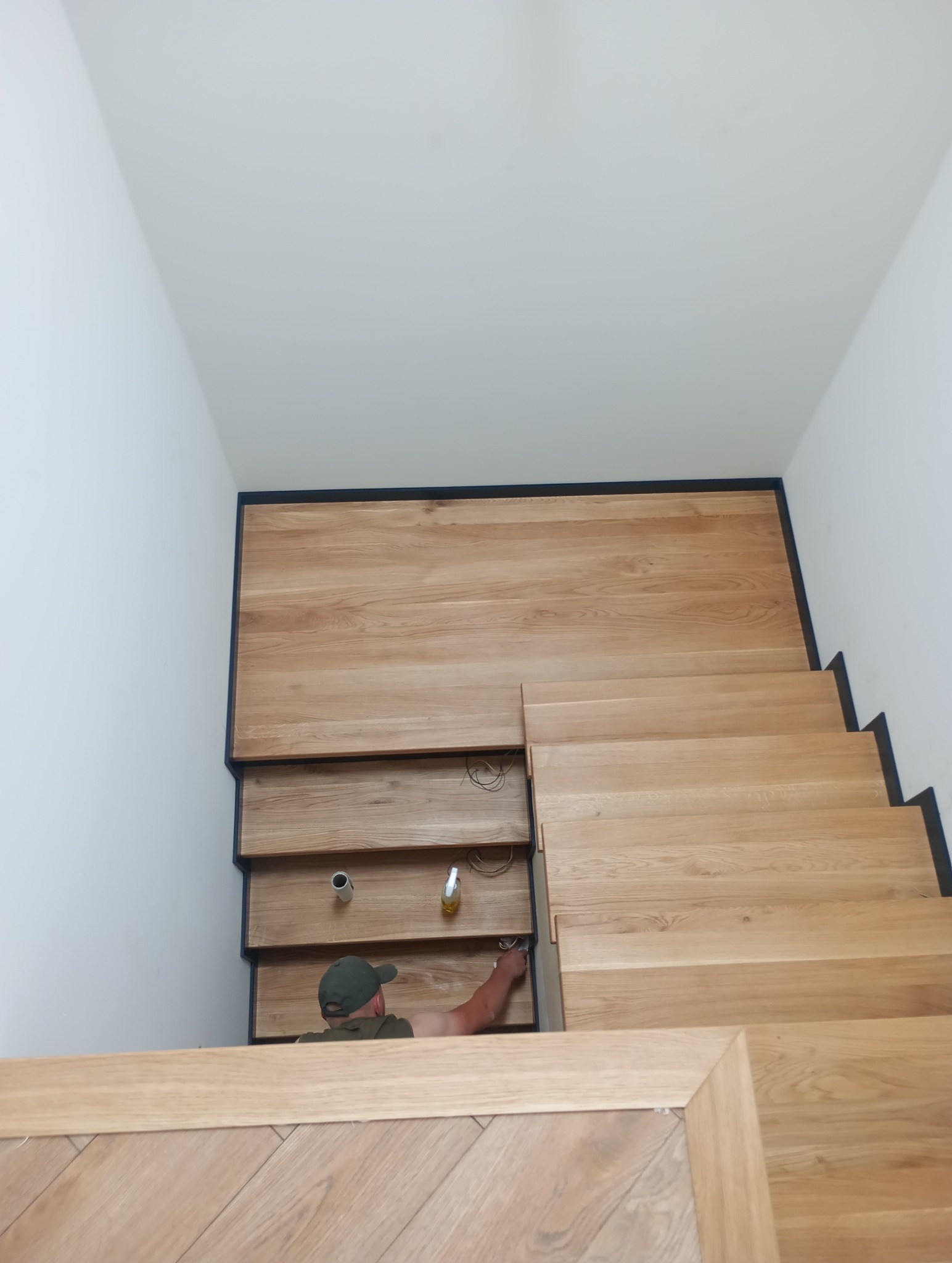 Montaż drewnianych schodów z czarnymi akcentami; widoczny pracownik w trakcie wykańczania detali.