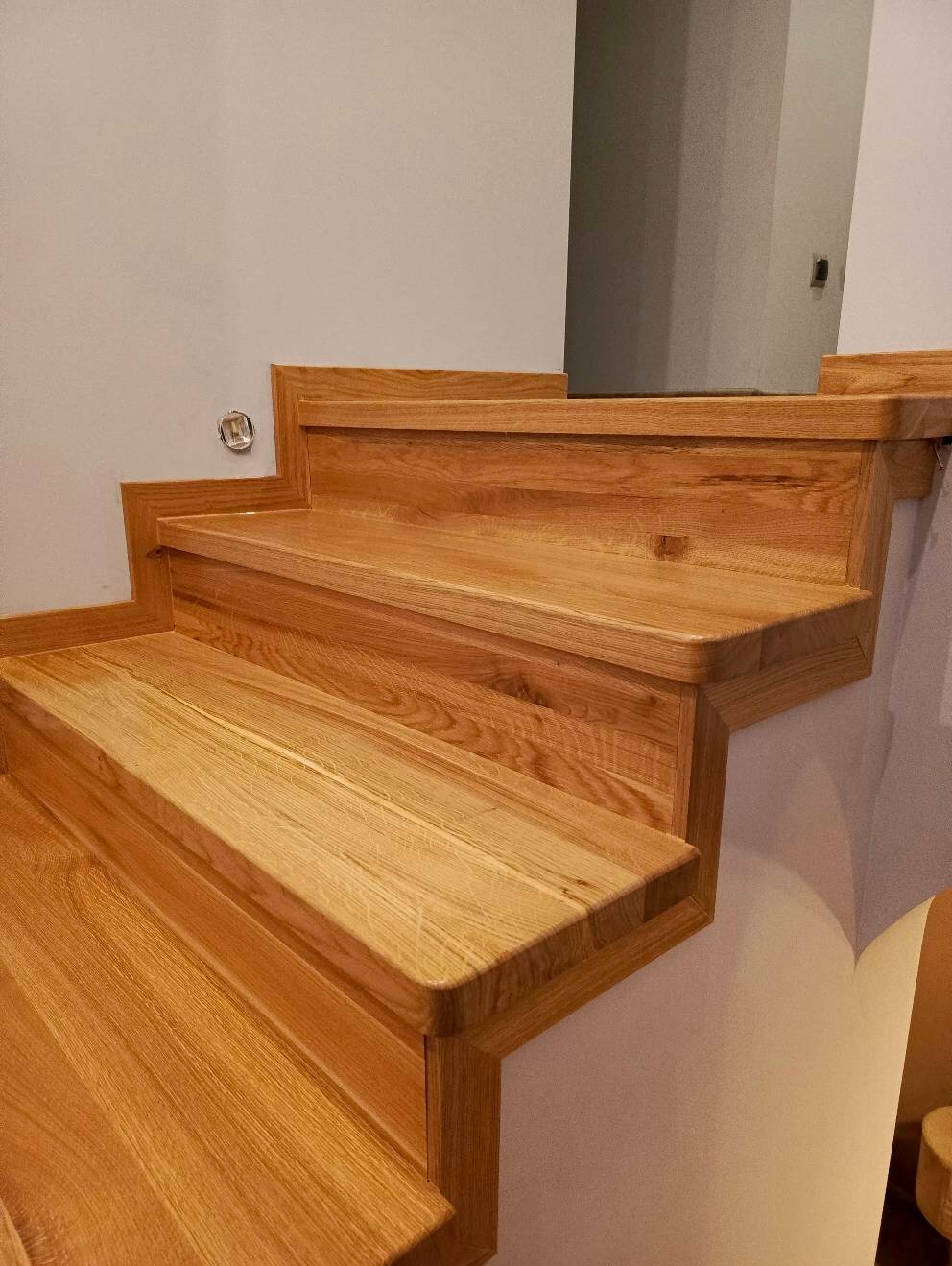 Dębowe stopnie schodowe z zaokrąglonymi krawędziami, widoczne z dołu, z gładkim wykończeniem i subtelnym usłojeniem drewna.