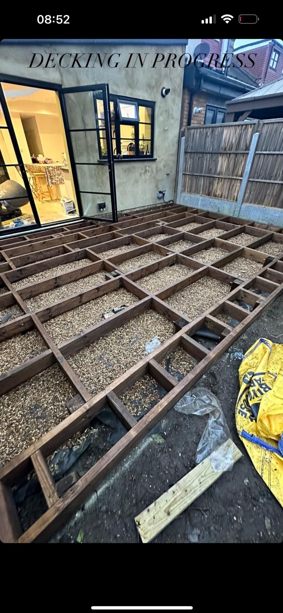 Konstrukcja pod taras z drewnianych belek wypełniona drobnym żwirem, widok na otwarte drzwi tarasowe i okno domu.