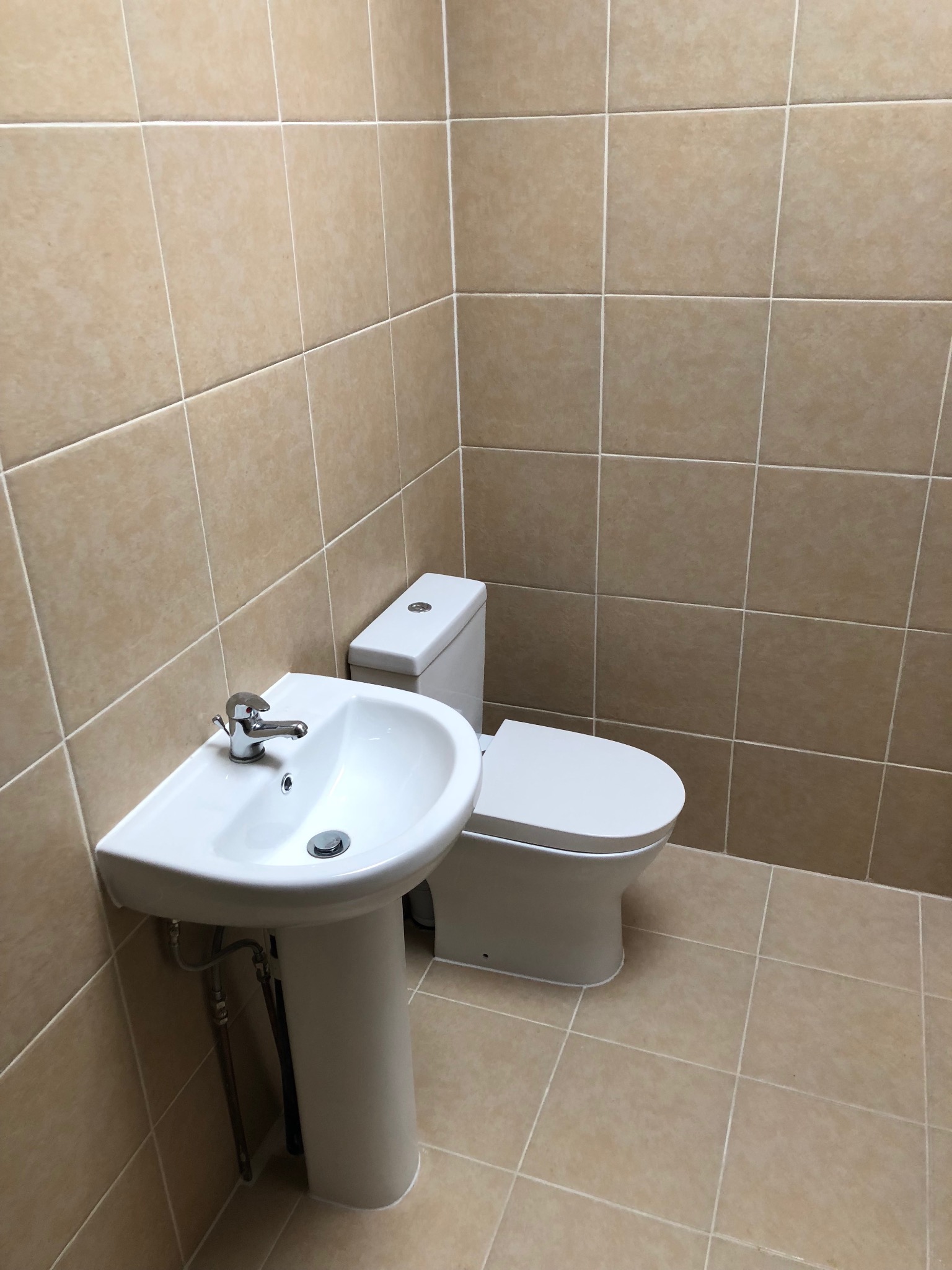 Nowa, czysta łazienka z beżowymi płytkami, białą umywalką na postumencie i toaletą, widok z niskiego kąta.