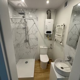 Well Done Krystian Chojnicki - Nowoczesna, wąska łazienka z kabiną prysznicową, umywalką nablatową, toaletą i podgrzewaczem wody, wykończona płytkami imitującymi marmur i drewnopodobnymi.