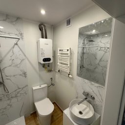 Well Done Krystian Chojnicki - Nowoczesna łazienka z marmurowymi płytkami, wiszącą umywalką, grzejnikiem drabinkowym i piecem gazowym Junkers.