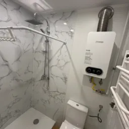 Nowoczesna łazienka z kabiną prysznicową wyłożoną płytkami imitującymi marmur, podwieszanym bojlerem Junkers i grzejnikiem drabinkowym.