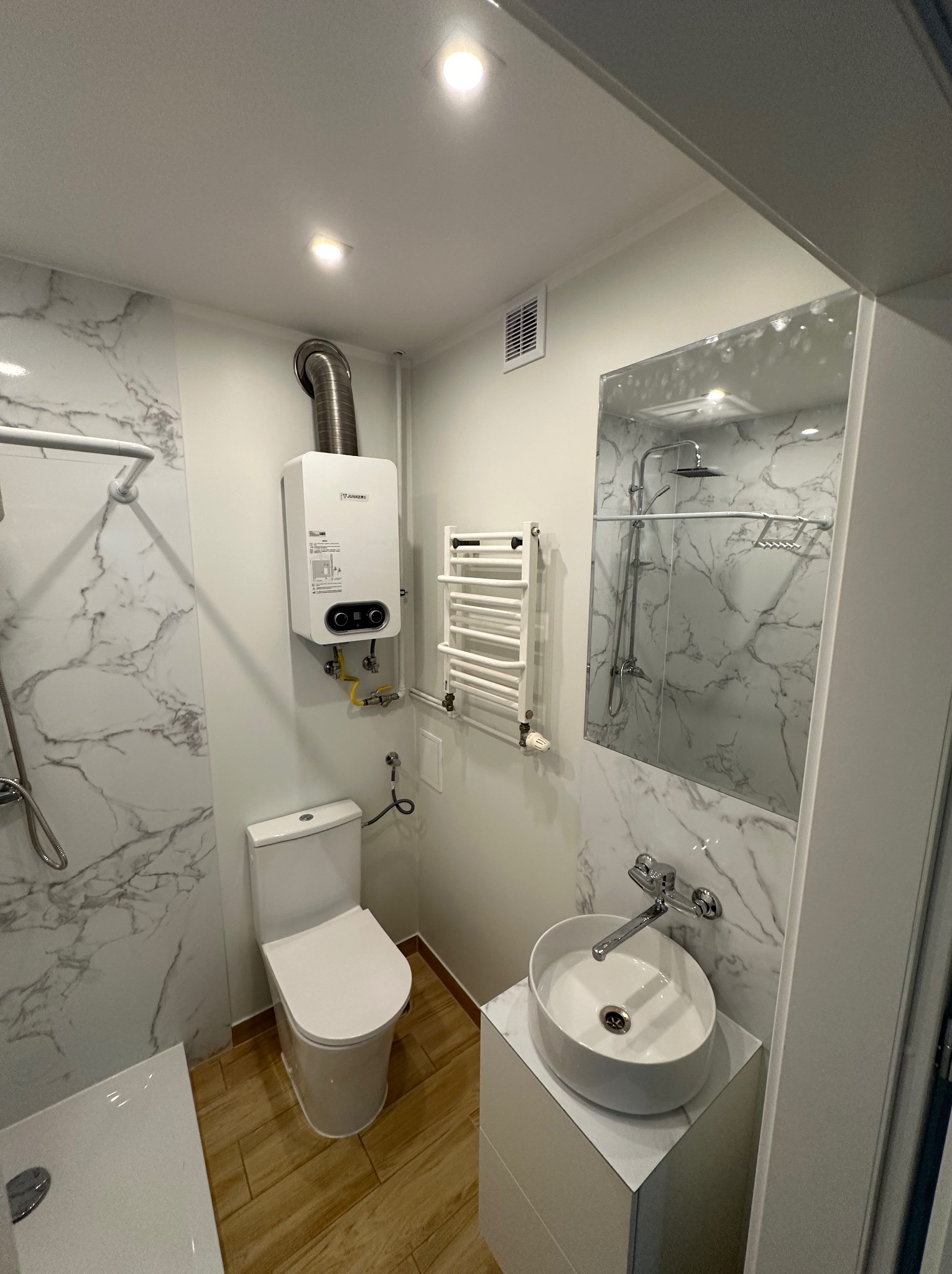 Nowoczesna łazienka z marmurowymi płytkami, wiszącą umywalką, grzejnikiem drabinkowym i piecem gazowym Junkers.