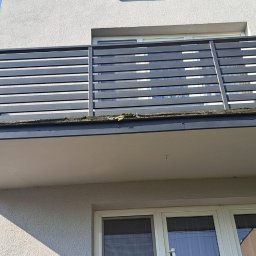 RafalK wykonczenia - Szary balkon z poziomymi szczebelkami, widok z dołu, z numerem '2' na ścianie budynku. Widoczne okna i fragment nieba.