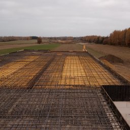 Kambud - Zbrojenie stropu domu murowanego z widocznym deskowaniem i siatką prętów stalowych na tle jesiennego krajobrazu.