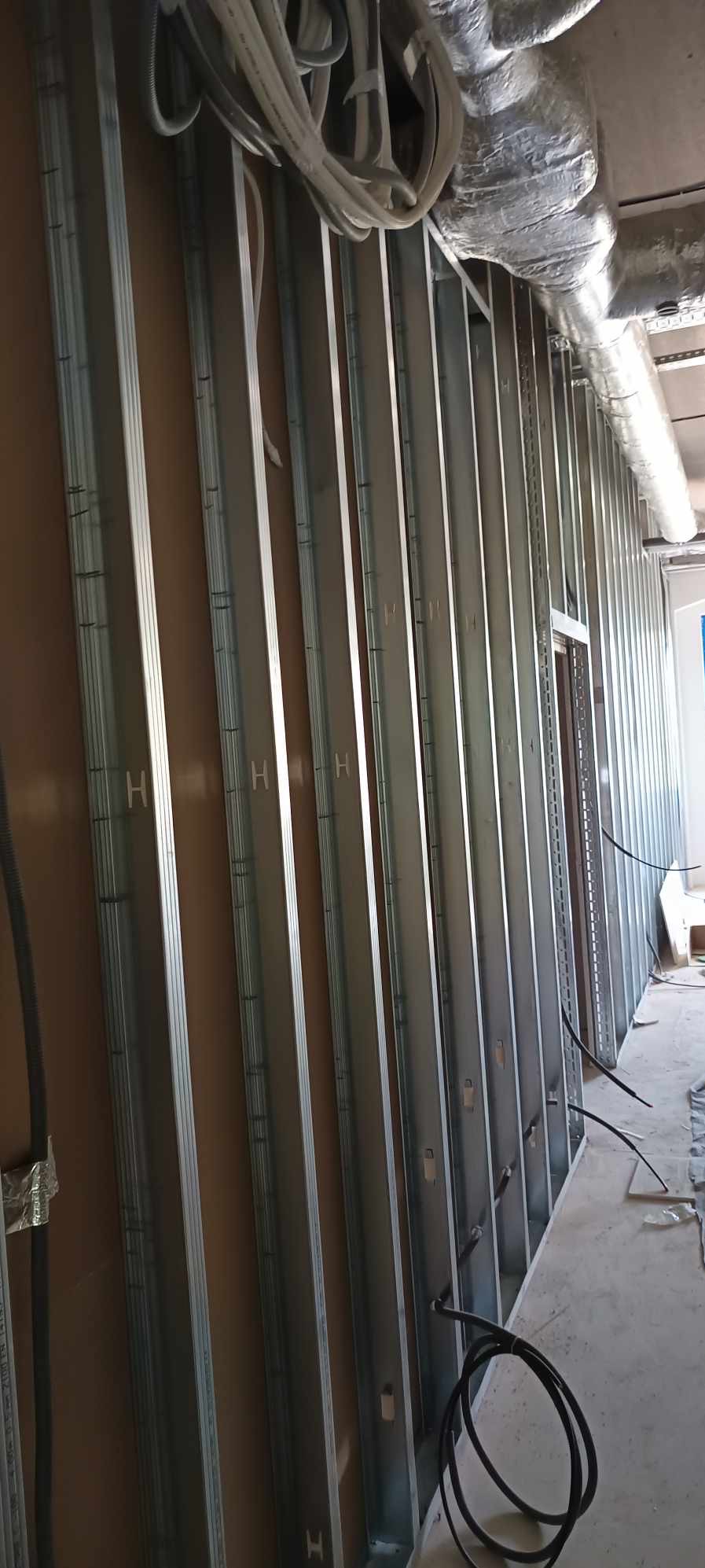 Metalowa konstrukcja szkieletowa ściany z widocznymi profilami pionowymi i przewodami instalacji elektrycznej, przygotowana do montażu okładzin.