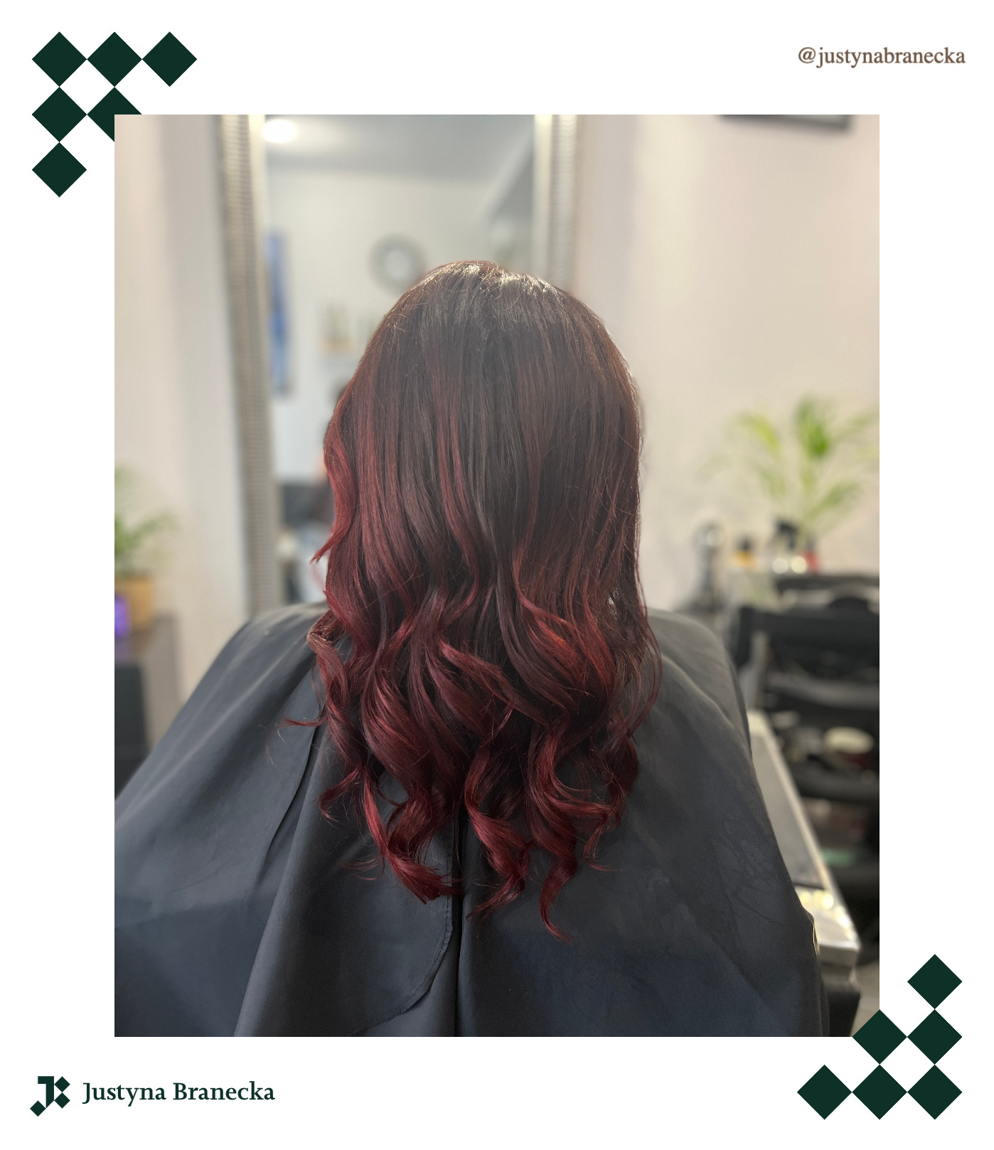 Widok z tyłu na ciemne, pofalowane włosy z czerwonymi refleksami, klientka w czarnej pelerynie fryzjerskiej, w tle lustro i wyposażenie salonu.