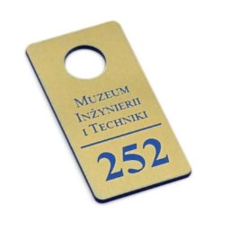 Strefaprezentacji.pl - Złota zawieszka na drzwi z niebieskim napisem 'Muzeum Inżynierii i Techniki' oraz numerem 252, zawieszka z otworem na górze, leżąca ukośnie na białym tle.