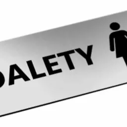 Szczotkowana metalowa tabliczka z napisem 'TOALETY' i piktogramami kobiety w sukience i mężczyzny, umieszczona pod kątem.