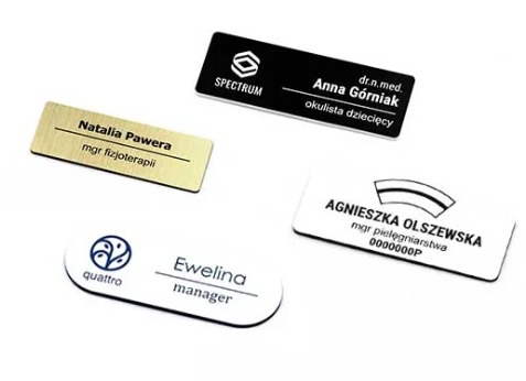 Zestaw czterech identyfikatorów imiennych w różnych stylach: czarny z logo Spectrum, złoty szczotkowany dla mgr fizjoterapii, biały z logo Quattro dla managera, oraz biały z ozdobnym paskiem...