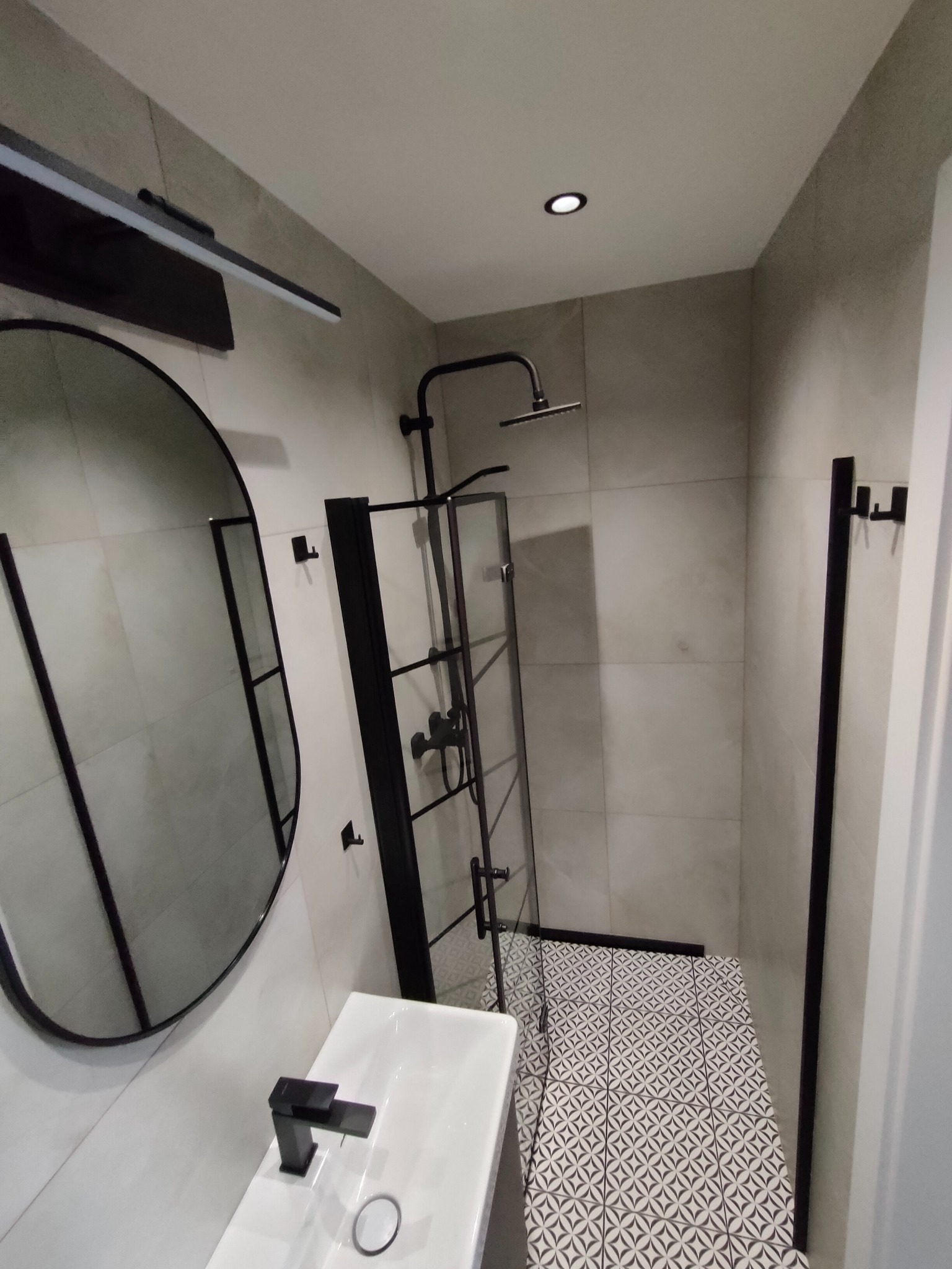 Nowoczesna łazienka po remoncie w Jaworzynie Śląskiej. Kabina prysznicowa typu walk-in z czarnymi profilami, okrągłe lustro i biała umywalka nablatowa.