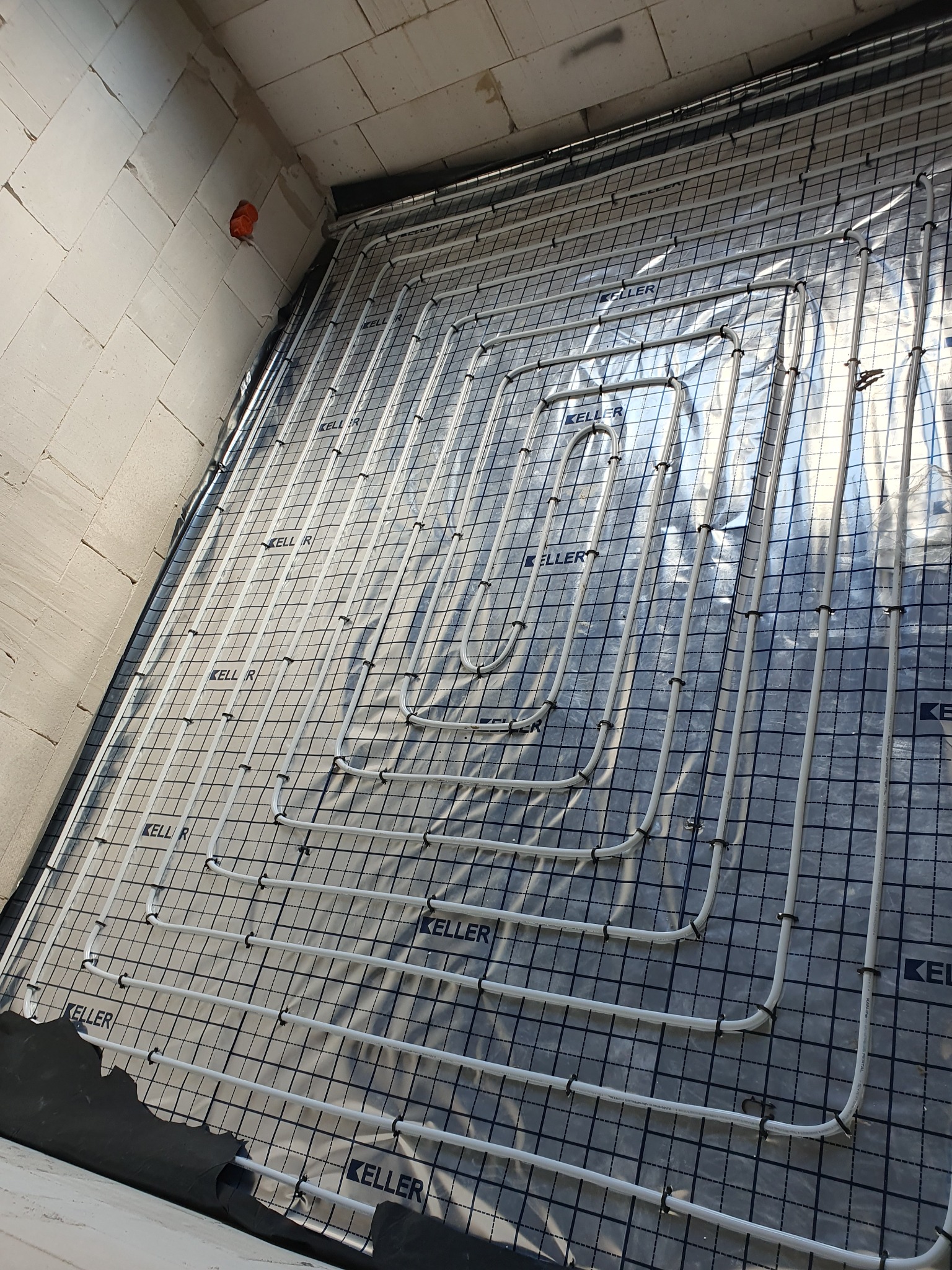 Układ rur ogrzewania podłogowego na folii z nadrukowanym logo, przed wylaniem wylewki, widok pod kątem w surowym wnętrzu.