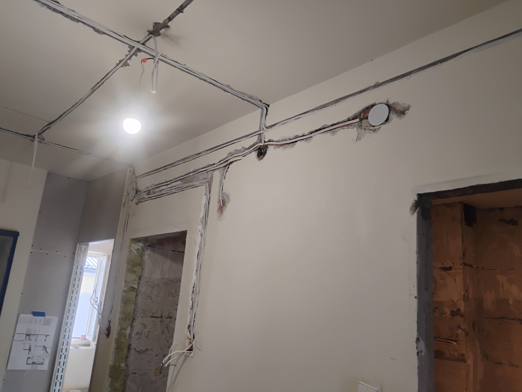 Rozprowadzenie instalacji elektrycznej po ścianach i suficie w trakcie prac wykończeniowych, widoczne kable w korytach i puszka pod gniazdko przed szpachlowaniem.