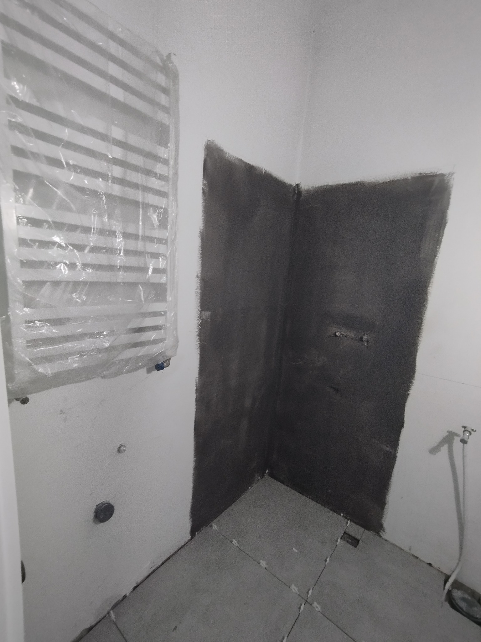 Przygotowanie łazienki do prac wykończeniowych: ściany po gruntowaniu, zabezpieczony folią grzejnik drabinkowy, ułożona podłoga z płytek gresowych.