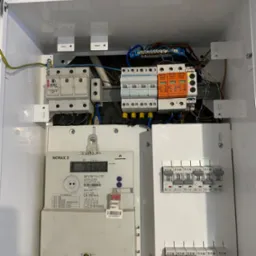 Zamknięta skrzynka elektryczna z licznikiem Norax 3, zabezpieczeniami Pro-Tec i wyłącznikami Eaton. Widoczne przewody i elementy instalacji elektrycznej.