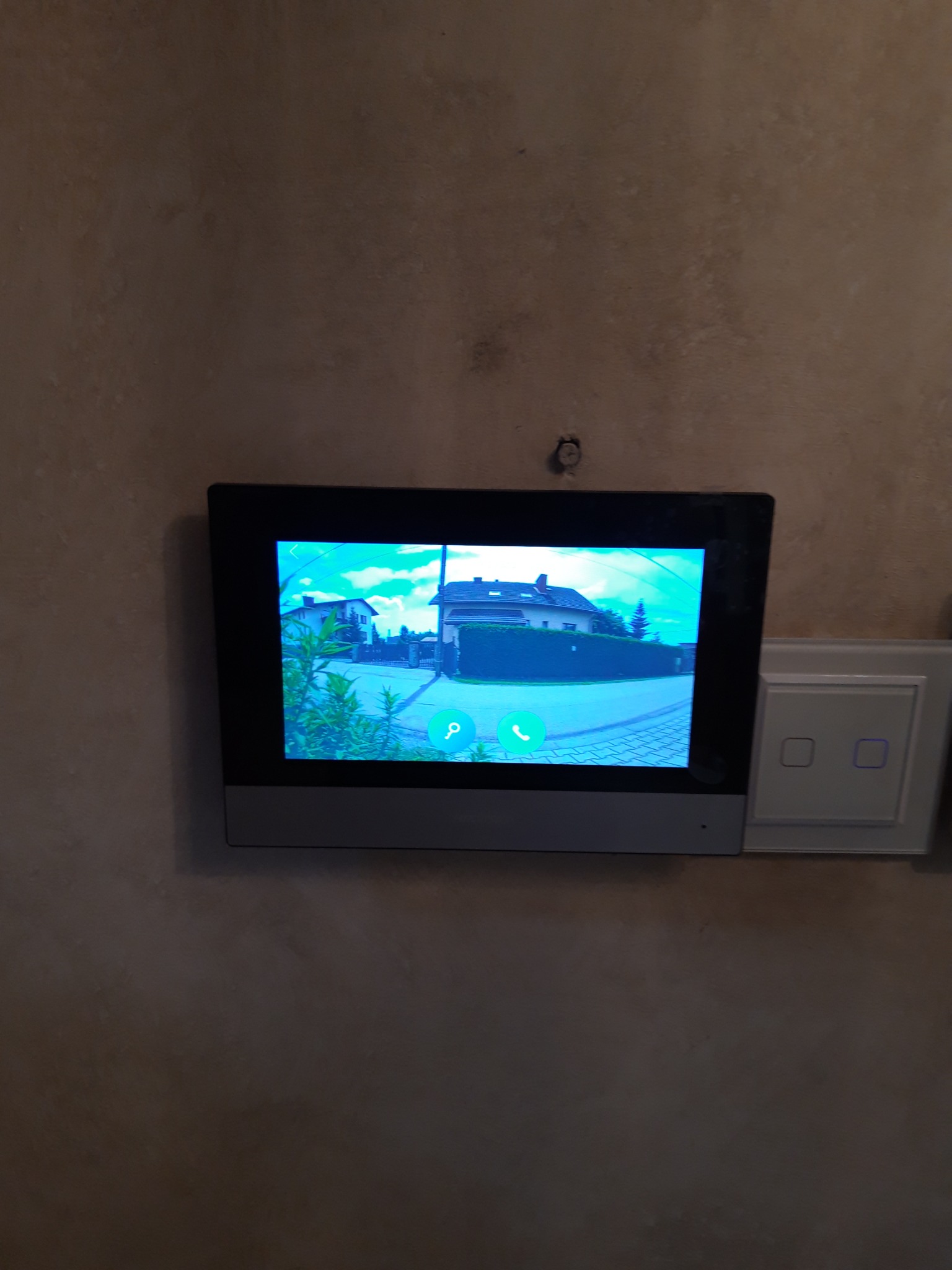 Zamontowany wideodomofon z podglądem na posesję, obok włącznik światła, widoczne ślady po montażu na ścianie.