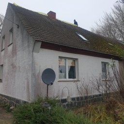 Dach i naprawa - Dom jednorodzinny z częściowo zdjętym starym pokryciem dachowym, widoczna żółta membrana dachowa i pracownik na dachu. Część dachu pokryta mchem.