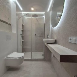 Master bud I Prace remontowe I Budownictwo I Warszawa - Nowoczesna łazienka w odcieniach szarości z podświetlanym lustrem, wiszącą toaletą i kabiną prysznicową typu walk-in, oświetlenie LED na suficie i ścianach.