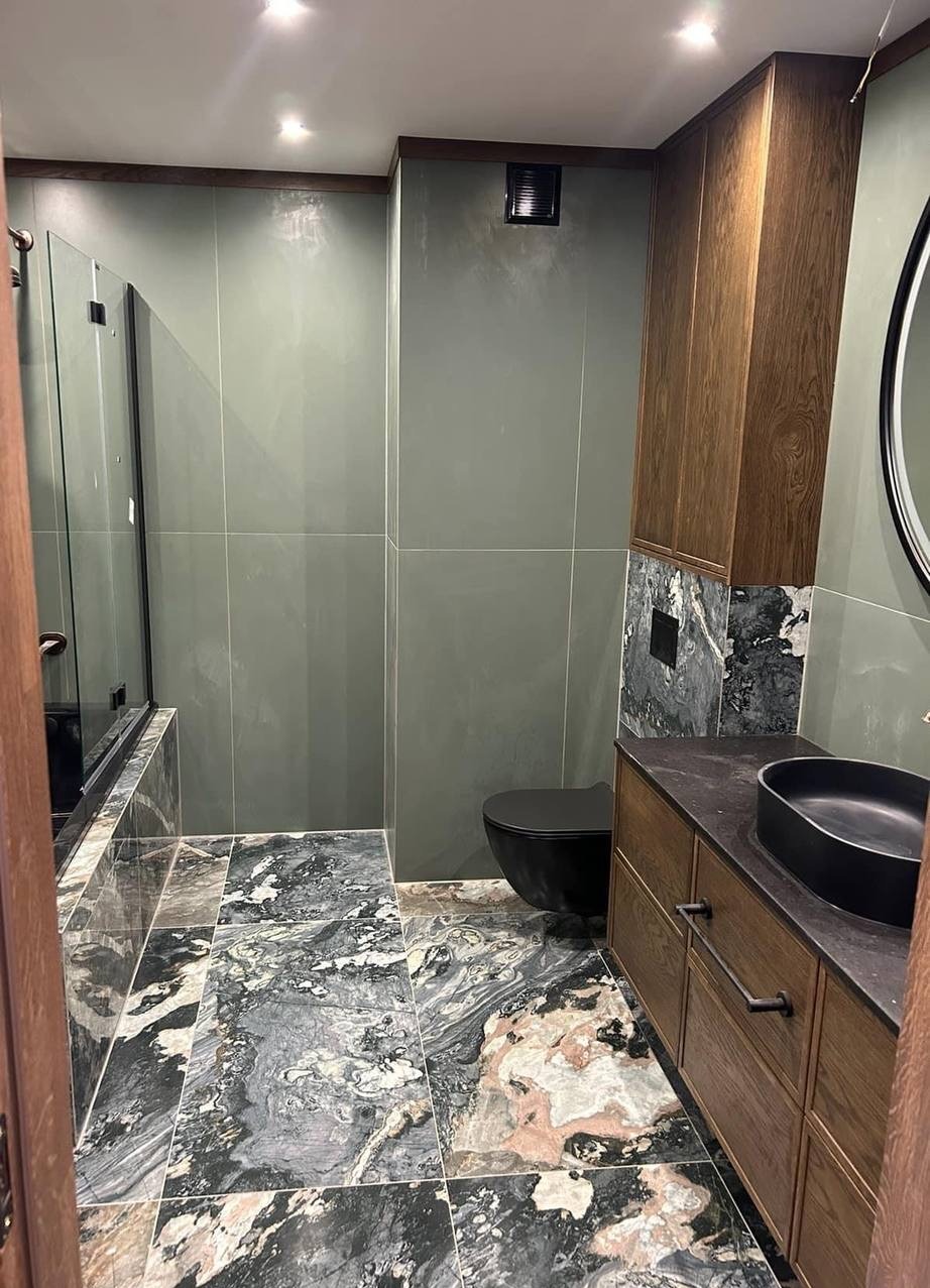 Nowoczesna łazienka w Warszawie z zielonymi płytkami ściennymi, marmurową podłogą, zabudową z drewnianymi szafkami i czarną armaturą.