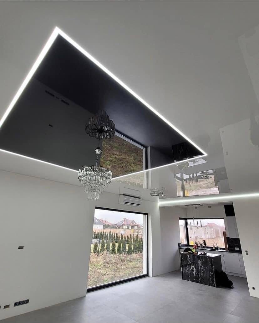 Nowoczesne wnętrze z czarnym, podwieszanym sufitem z oświetleniem LED, kryształowym żyrandolem i widokiem na ogród przez duże okno.