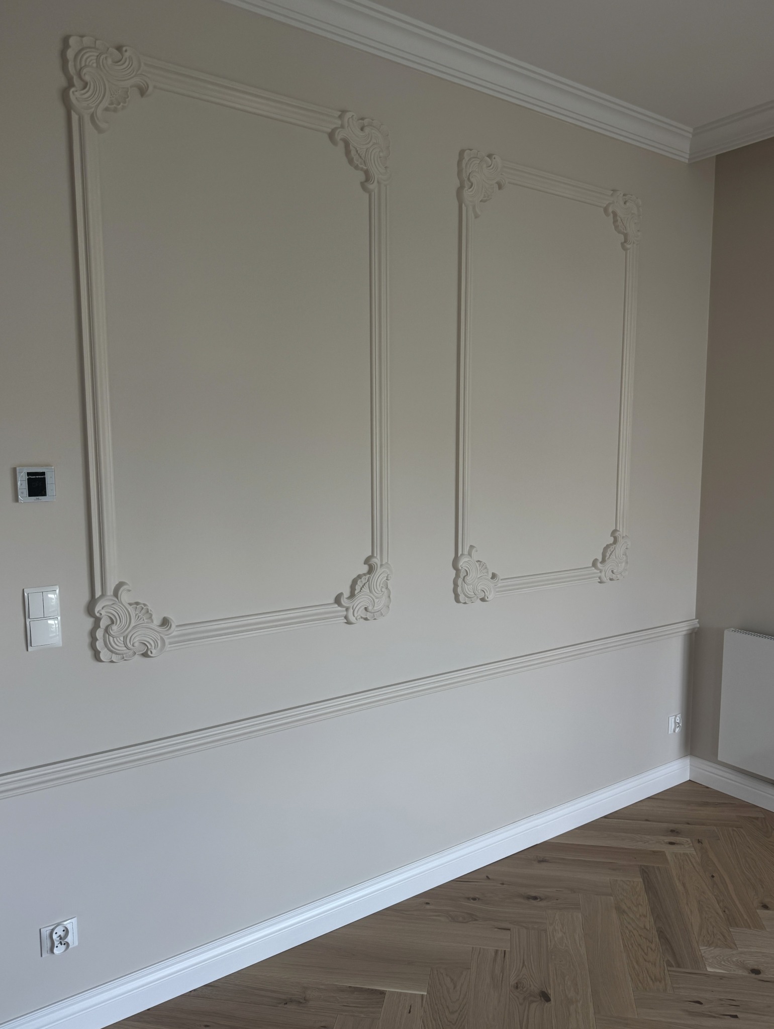 Eleganckie wykończenie ścian z dekoracyjnymi, kremowymi listwami w kształcie prostokątów z ornamentami w rogach, uzupełnione listwą przypodłogową i parkietem.