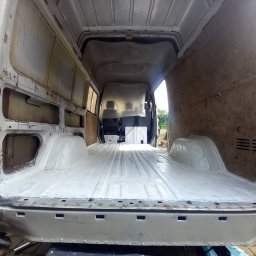 RRR Renowacja - Wnętrze furgonetki w trakcie renowacji, widok z tyłu na odświeżoną, pomalowaną na biało podłogę, surowe ściany boczne bez tapicerki, widoczne ślady korozji i spawania na karoserii.