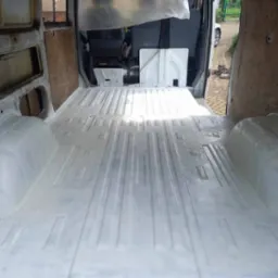 Wnętrze furgonetki po nałożeniu białej powłoki antykorozyjnej na podłogę i nadkola, widoczne ślady korozji na ścianach bocznych.