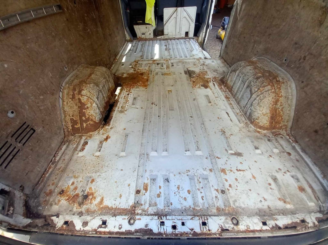 Wnętrze pordzewiałej furgonetki przed renowacją, widoczne liczne ogniska korozji na podłodze i ścianach, surowe warunki eksploatacji.