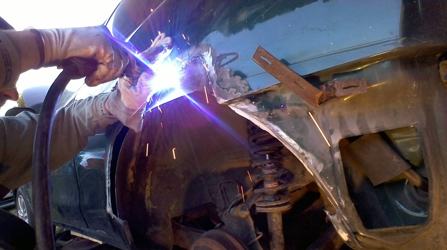 Spawanie nadkola samochodu z widocznymi iskrami i spawarką w rękach spawacza w rękawicach ochronnych.