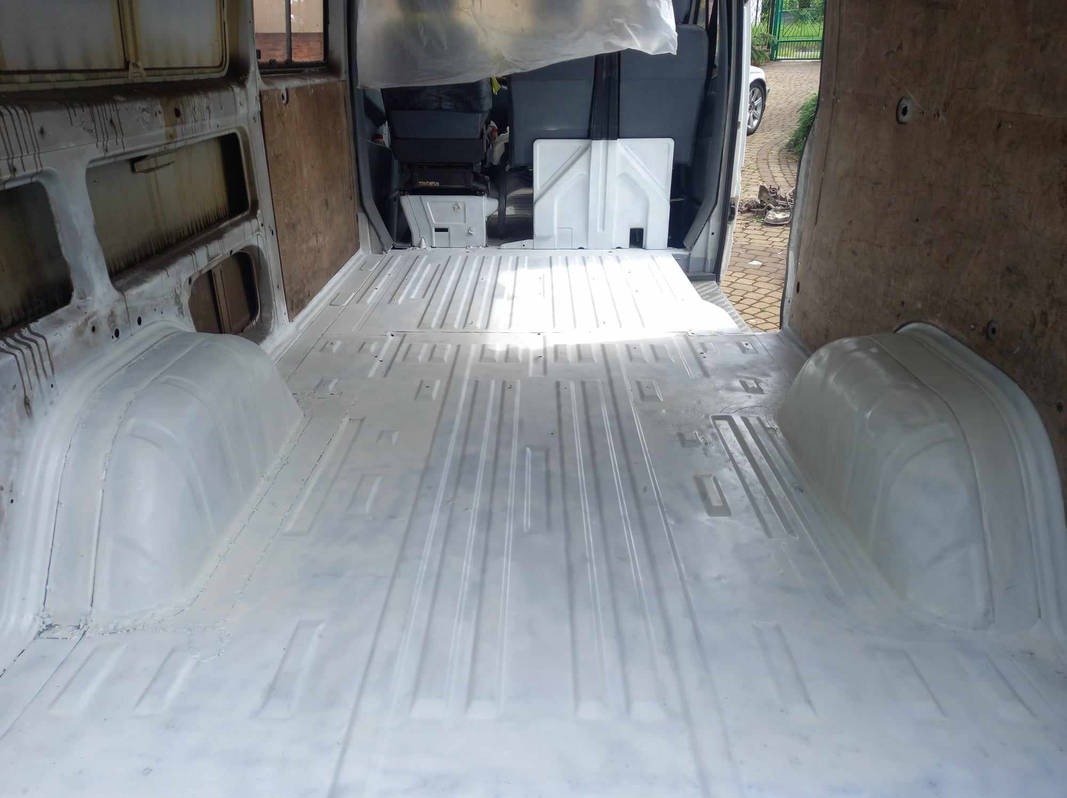 Wnętrze furgonetki po nałożeniu białej powłoki antykorozyjnej na podłogę i nadkola, widoczne ślady korozji na ścianach bocznych.