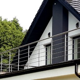 INOX-STAL SC - Balkon z nowoczesną balustradą nierdzewną, widok z zewnątrz na tle domu z czarnym dachem i zielenią drzew.