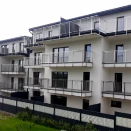 Nowoczesny apartamentowiec z balkonami zabezpieczonymi prostymi, metalowymi balustradami, widoczne z poziomu terenu.