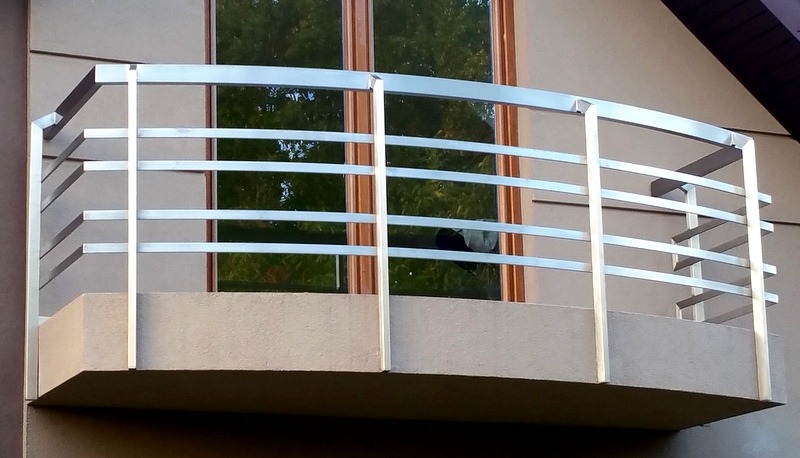 Nowoczesna balustrada balkonowa ze stali nierdzewnej z poziomymi poprzeczkami, widok z zewnątrz na tle okna z zielonym odbiciem.