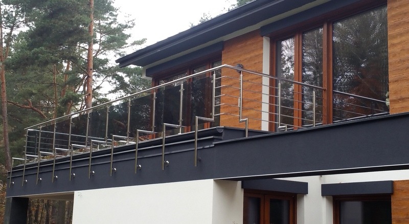 Nowoczesna balustrada ze stali na balkonie domu z drewnianą elewacją i dużymi oknami.