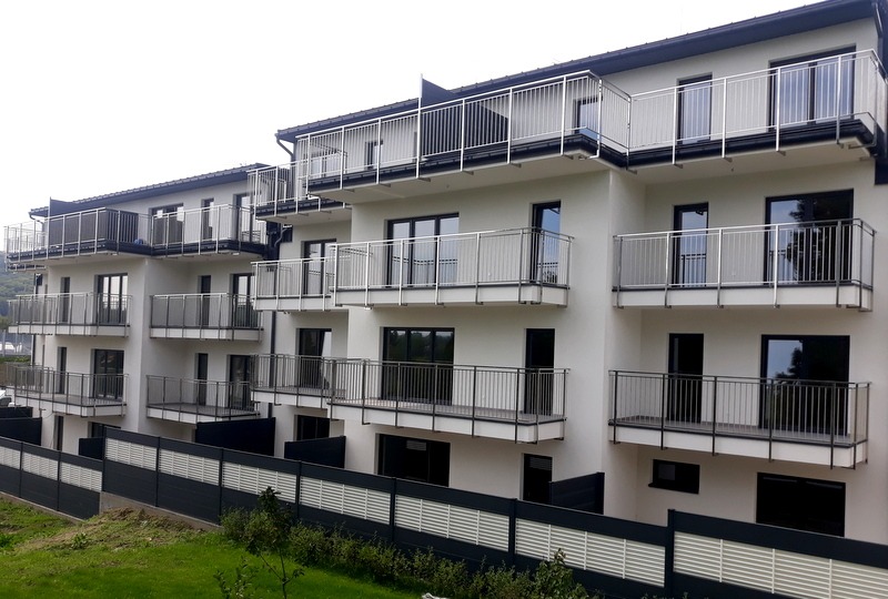 Nowoczesny apartamentowiec z balkonami zabezpieczonymi prostymi, metalowymi balustradami, widoczne z poziomu terenu.