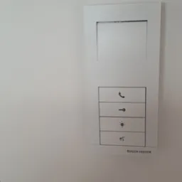 Panel sterowania inteligentnego domu Busch-Jaeger z przyciskami do sterowania oświetleniem, domofonem i innymi funkcjami, zamontowany na białej ścianie.