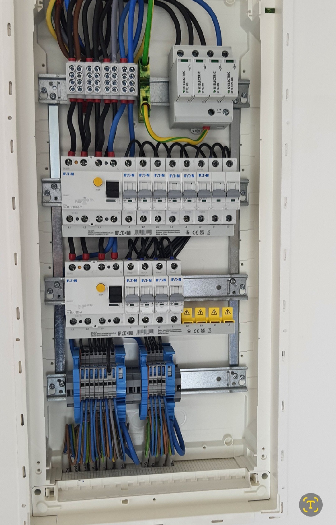 Rozdzielnia elektryczna z zainstalowanymi zabezpieczeniami i podłączonymi przewodami, widoczne komponenty marki Eaton i K'Electric, przewody w różnych kolorach uporządkowane w listwach zaciskowych.