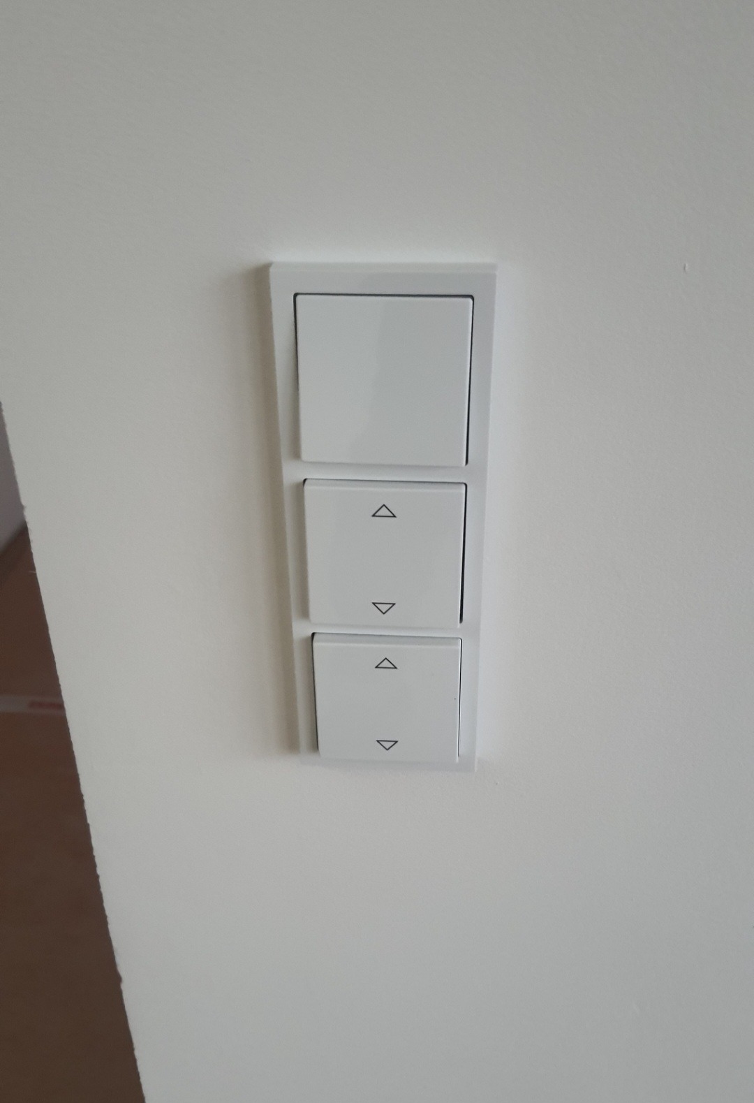 Panel z trzema białymi przełącznikami na ścianie, z symbolami strzałek góra-dół na dwóch dolnych, prawdopodobnie do sterowania roletami.